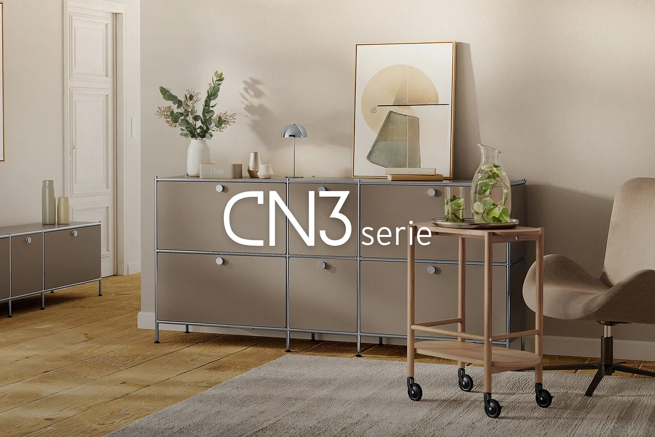 Modernes Wohnzimmer mit großem, taupefarbenem modularem Sideboard, dekoriert mit Vase, Lampe und Kunst. Rechts ein Servierwagen mit Wasserkaraffe und Sessel auf einem Teppich. Links ein kleineres Sideboard. Text: CN3 serie.