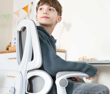 Junge sitzt auf einem weißen Bürostuhl und schaut nach oben. Im Hintergrund sind Spielzeuge und eine bunte Girlande zu sehen.