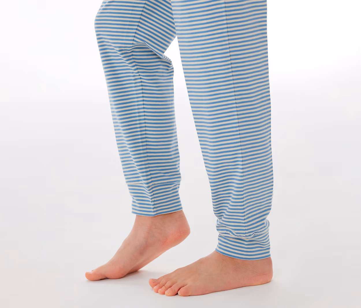 Kinderbeine und nackte Füße, die eine SCHIESSER Kinder-Pyjamahose mit blau-weißen Streifen tragen.
