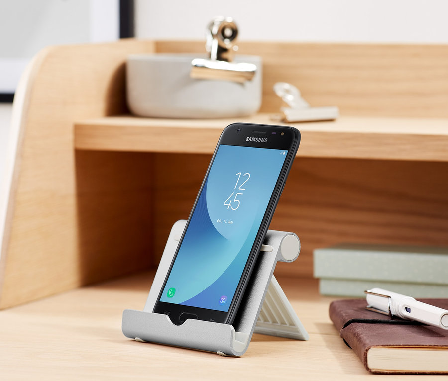 Schwarzes Smartphone steht in einer Smartphone- und Tablet-Halterung auf einem Schreibtisch.
