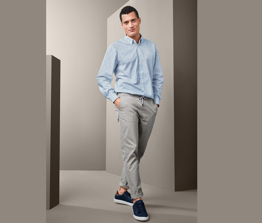 Mann posiert in einem Hemd mit Button-down-Kragen, Comfort Fit, grauer Hose und blauen Schuhen.