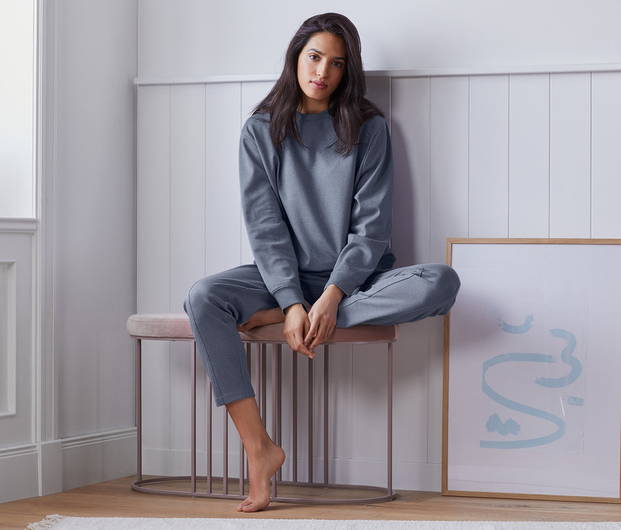 Frau sitzt in einem Loungewear-Sweater und Hose auf einem Hocker.