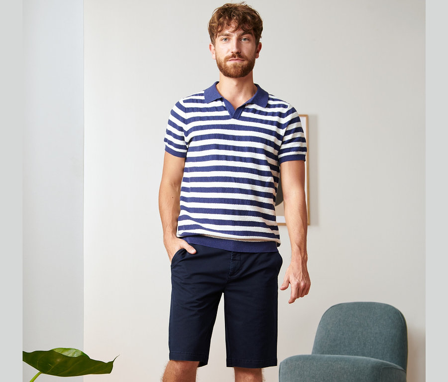 Ein Mann steht und trägt marineblaue Chino-Shorts und ein gestreiftes Poloshirt.