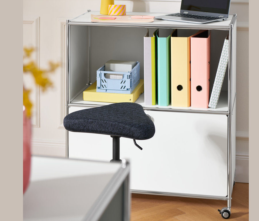 Auf einem Sideboard »CN3« mit Klappfach stehen ein Laptop, Ordner und ein gelber Organizer. Davor steht ein Topstar Ergo-Hocker »Sitness H1«.