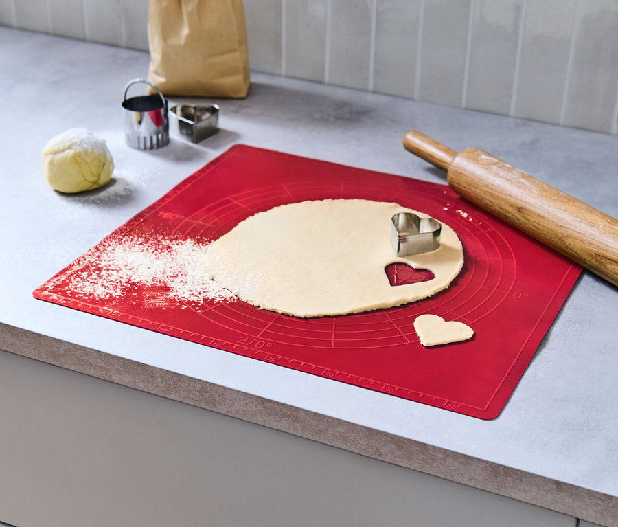 Teig wird auf einer roten Dauerbackmatte ausgerollt und mit einem herzförmigen Ausstecher bearbeitet.