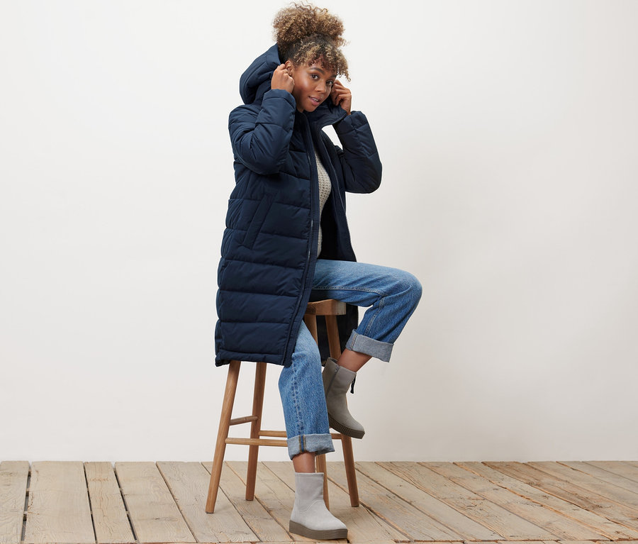 Eine Frau sitzt auf einem Hocker und trägt einen blauen Steppmantel.