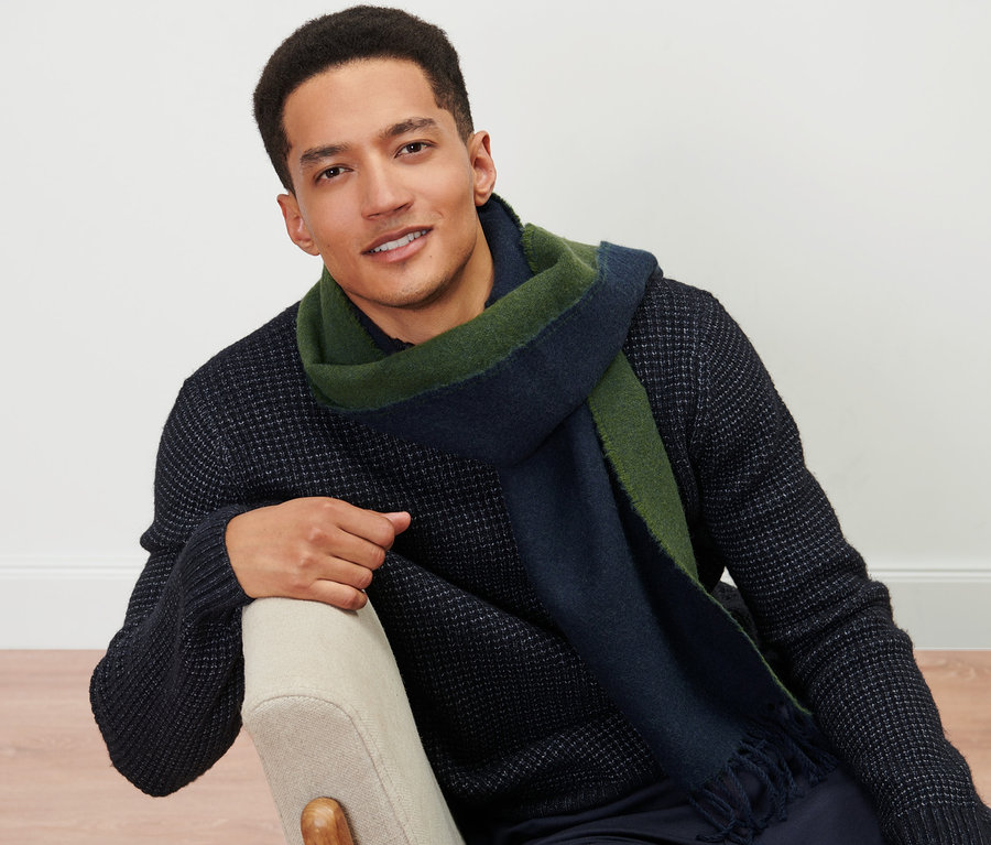 Mann sitzt auf einem Stuhl und trägt einen Webschal.