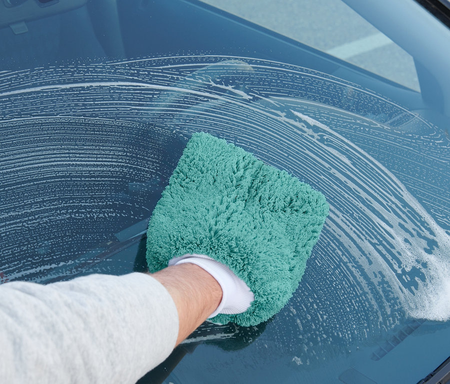 Mann wischt mit einem Auto-Waschhandschuh die Windschutzscheibe eines Autos.