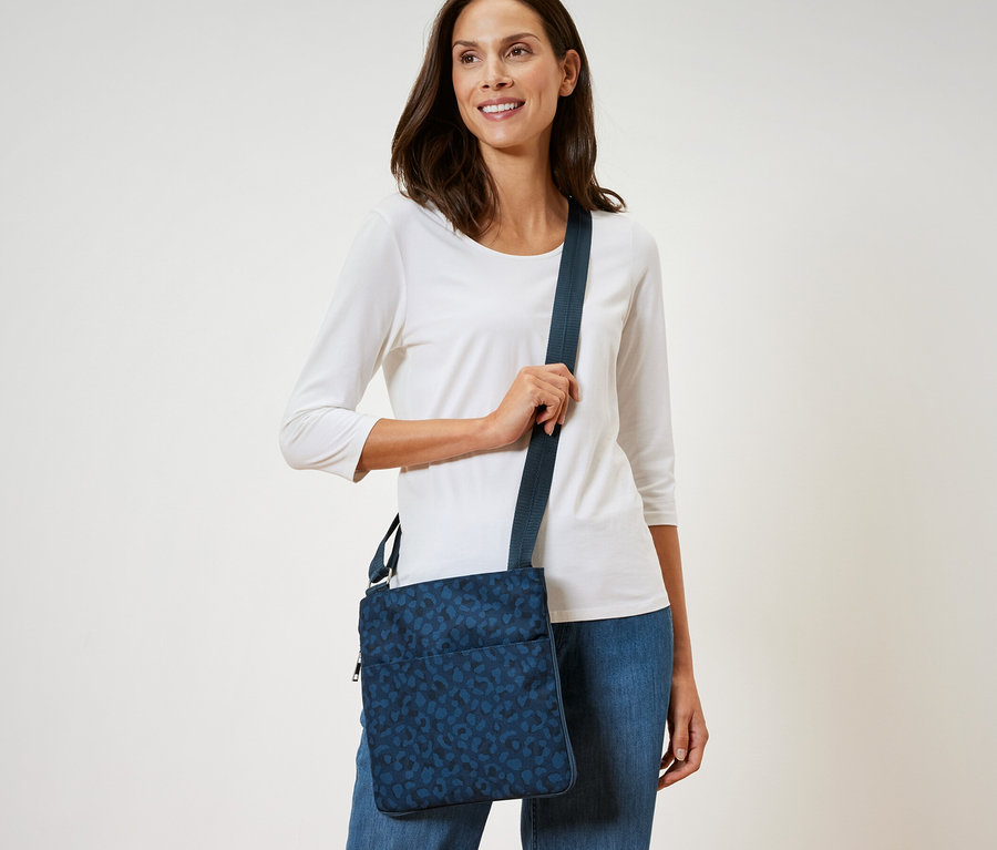 Frau mit dunklen Haaren und weißem Hemd posiert mit einer blauen Sicherheits-Umhängetasche.