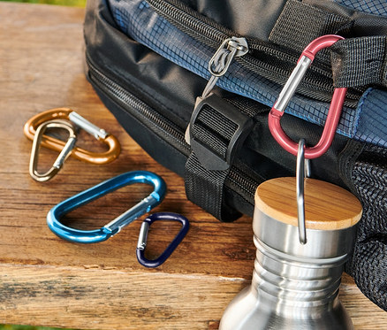 Blauer Rucksack, eine Edelstahlflasche und 5 Karabinerhaken liegen auf einer Holzbank.