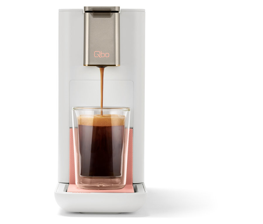 Kaffee wird aus einer Qbo ICONIC x Pantone Special Edition Muted Clay Kaffeemaschine in ein Glas gegossen.