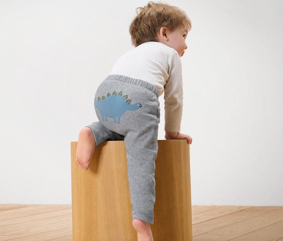 Ein Kind sitzt auf einem Holzwürfel und trägt eine graue Baby-Sweathose mit Dino.
