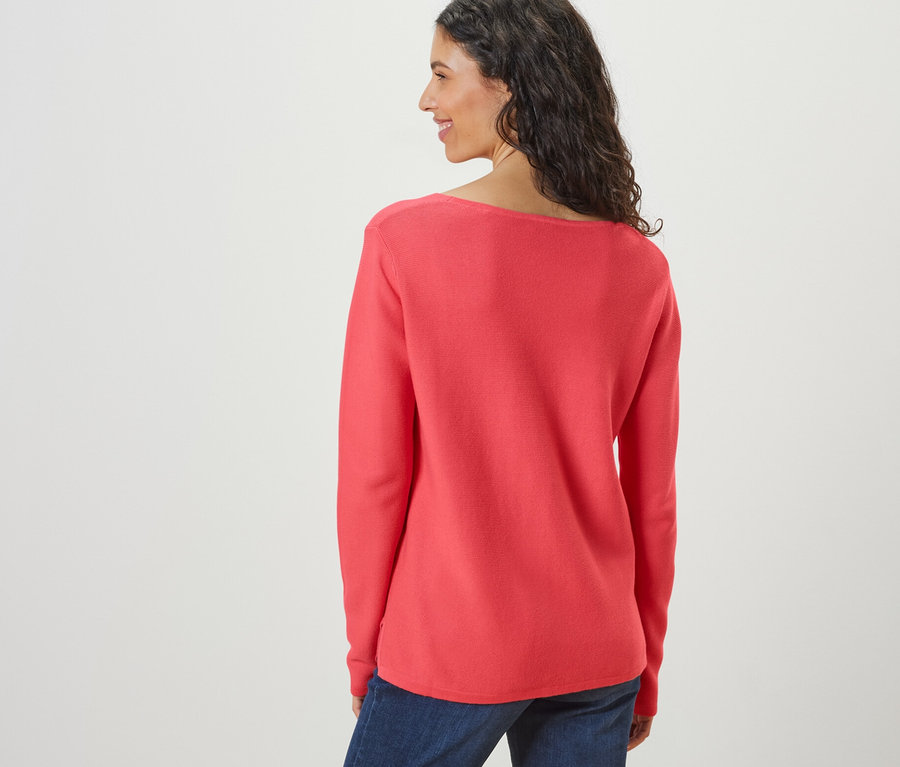 Frau schaut über die Schulter und trägt einen korallfarbenen Strickpullover.