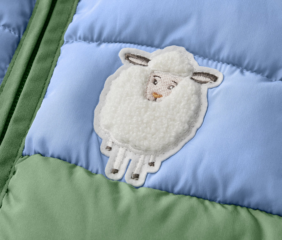 Detail einer Kinder-Steppweste im Colorblocking-Design mit einem Schaf-Applikation.