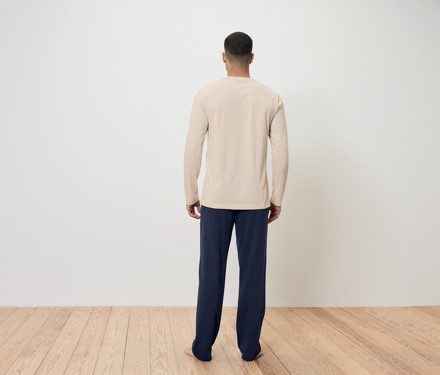 Ein Mann mit dem Rücken zur Kamera trägt ein beiges Langarmshirt und dunkelblaue Hosen.
