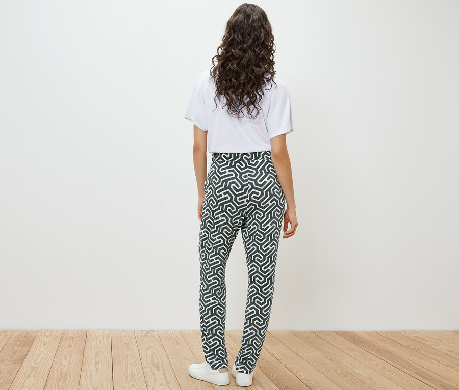 Rückansicht einer Frau in weißem T-Shirt und grüner bedruckter Jerseyhose.