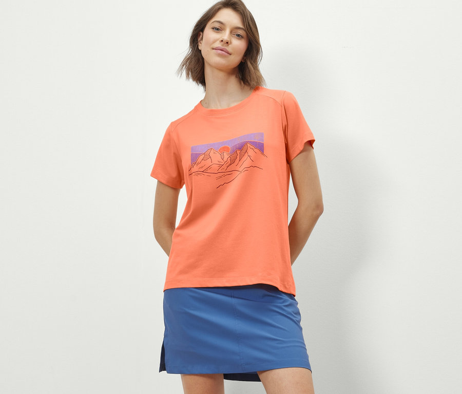 Frau trägt ein orangefarbenes T-Shirt mit Print und einen blauen Rock.