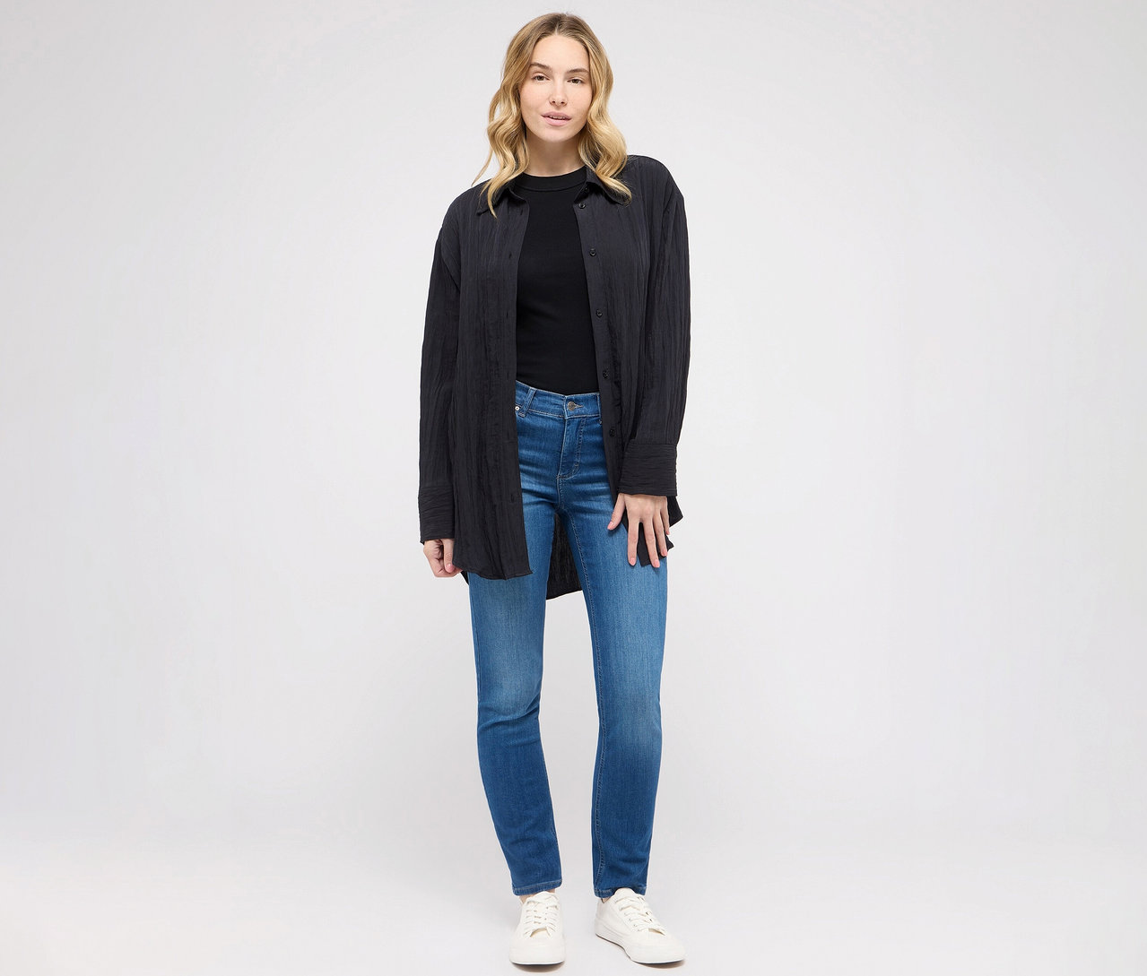 Frau posiert in Angels Jeans »Cici« Slim Fit, mid blue, schwarzem T-Shirt und Bluse.