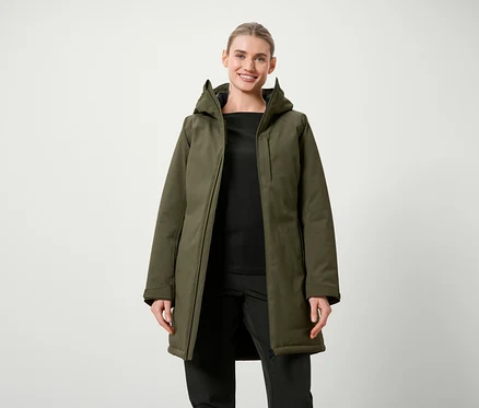 Frau posiert in olivgrüner Jacke mit Kapuze und schwarzer Kleidung.