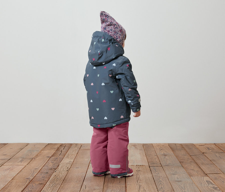 Rückansicht eines Kindes in einer Winterjacke mit Kapuze und Herzmuster und einer rosa Schneehose.