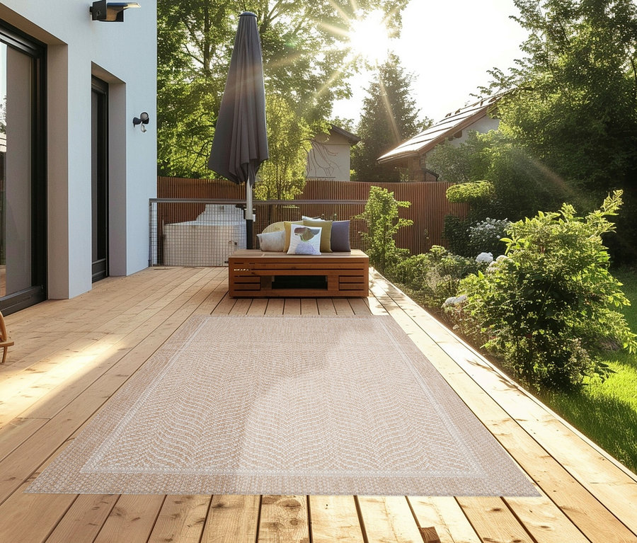 Ein beiger Teppich »Twine« mit Fischgrätenmuster liegt auf einer Holzterrasse neben einer Sitzecke.