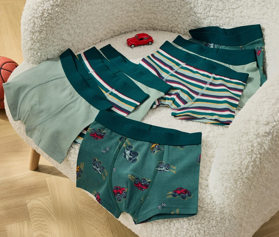 Auf einem flauschigen Stuhl liegen Kinderboxershorts und ein kleines rotes Spielzeugauto, daneben steht ein Basketball.
