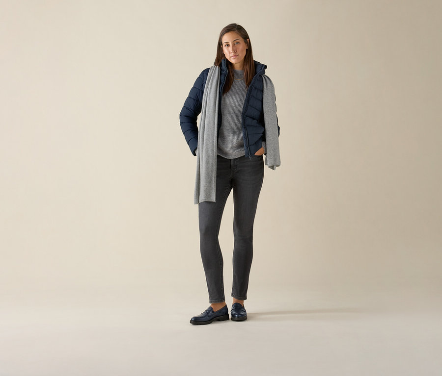 Frau steht und trägt eine Slim-Jeans – Fit »Emma« in Grey Denim, einen grauen Pullover, eine dunkelblaue Jacke und einen grauen Schal.