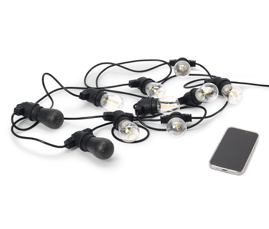 Eine schwarze LED-Outdoor-Lichterkette mit 2 Bluetooth®-Lautsprechern liegt neben einem Handy auf einem weißen Hintergrund.