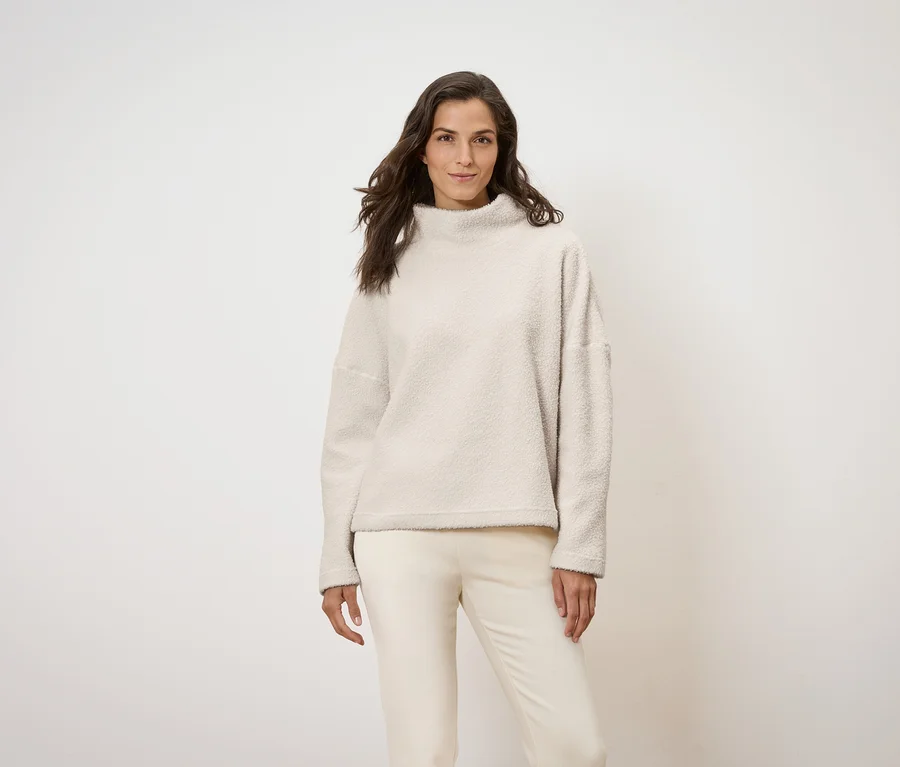 Frau posiert in cremefarbenem Pullover und Hose.