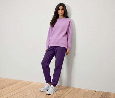 Eine Frau posiert in einem lila Sweatshirt und einer lila Jogginghose.