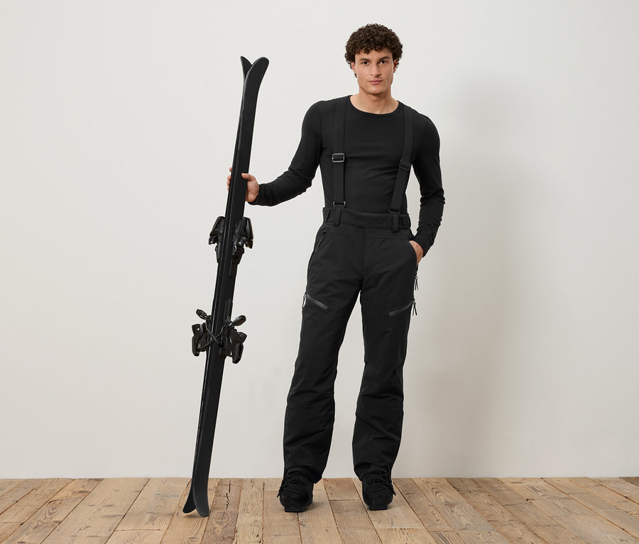 Mann in schwarzer Skibekleidung hält schwarze Skier.