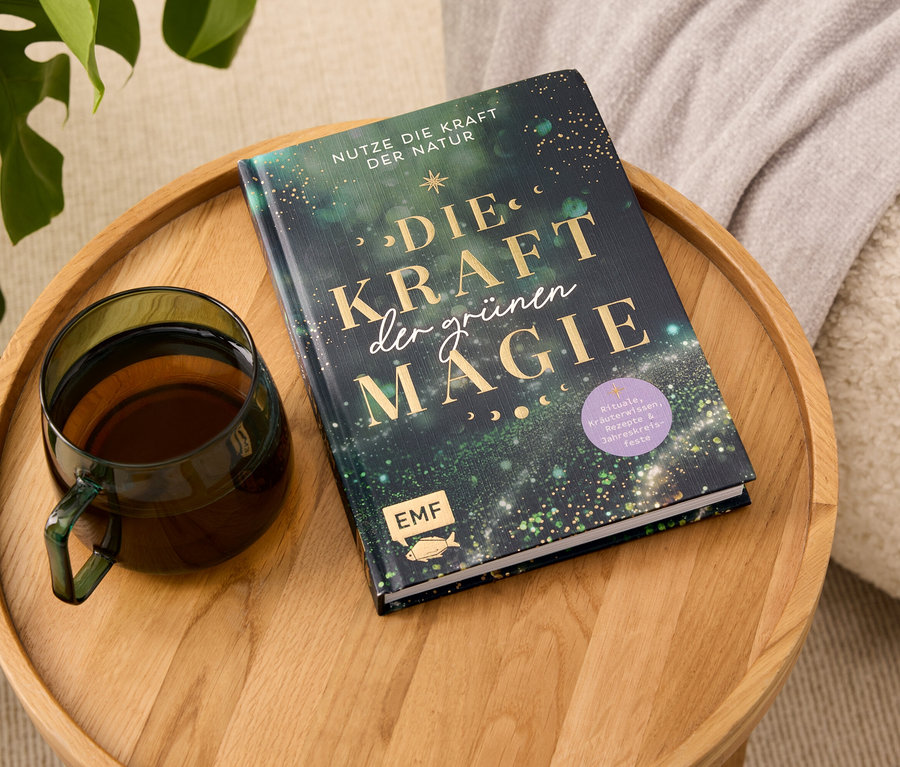 Auf einem Holztablett liegen ein Buch mit dem Titel "Die Kraft der grünen Magie" und eine gläserne Tasse mit Getränk.