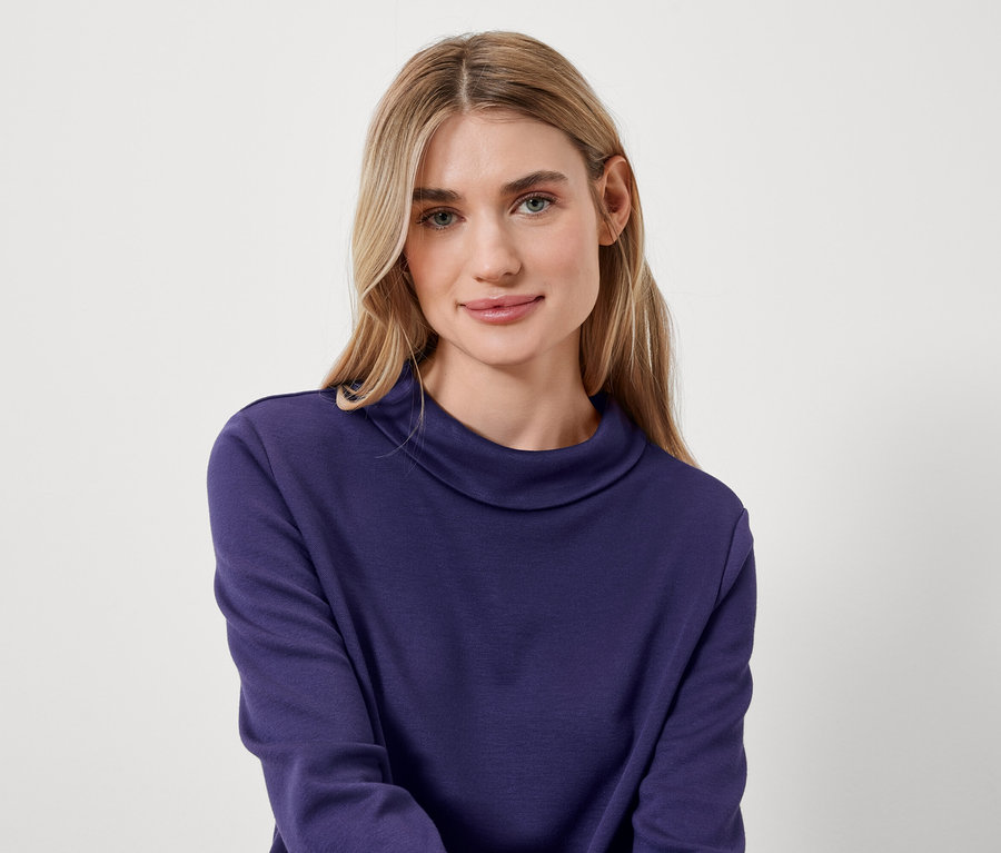 Porträt einer Frau mit blonden Haaren in einem blauen Rollkragenpullover.