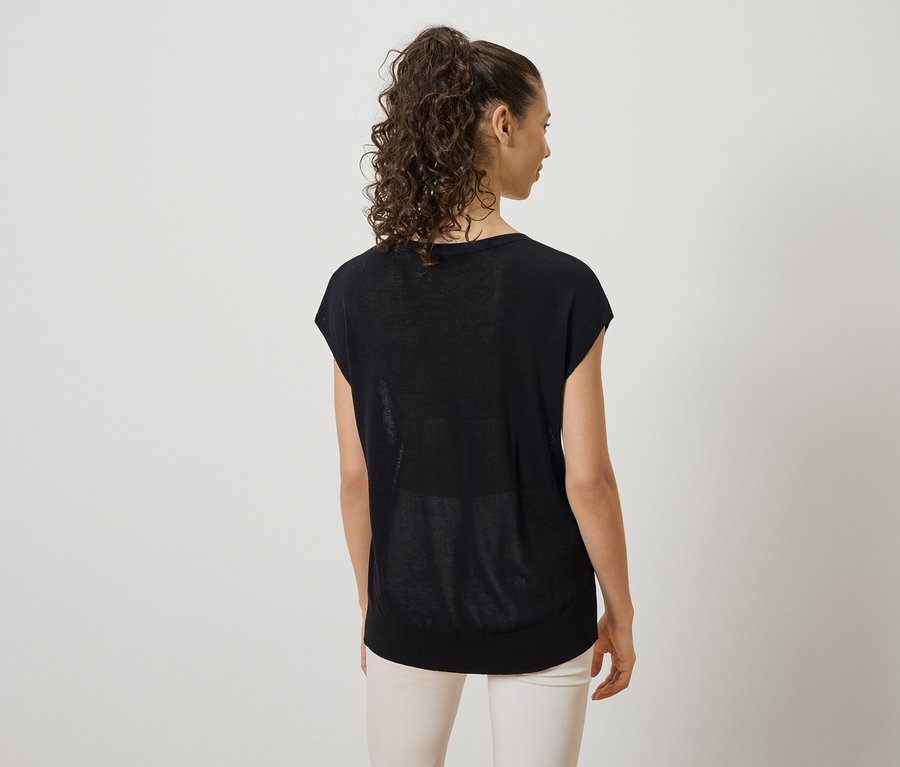 Frau mit lockigem Haar trägt ein schwarzes T-Shirt und eine helle Hose, von hinten fotografiert.