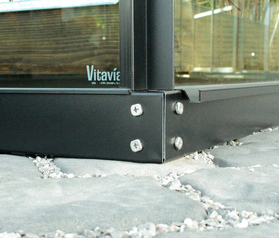 Nahaufnahme vom Rahmenfundament des Vitavia Gewächshauses Orion ESG 5 m², befestigt mit Schrauben auf Steinplatten.
