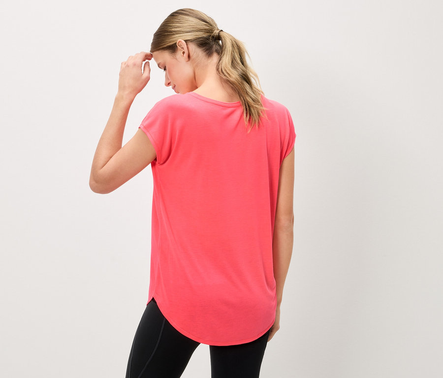 Frau von hinten in einem korallfarbenen T-Shirt und schwarzen Leggings, die ihre Stirn berührt.