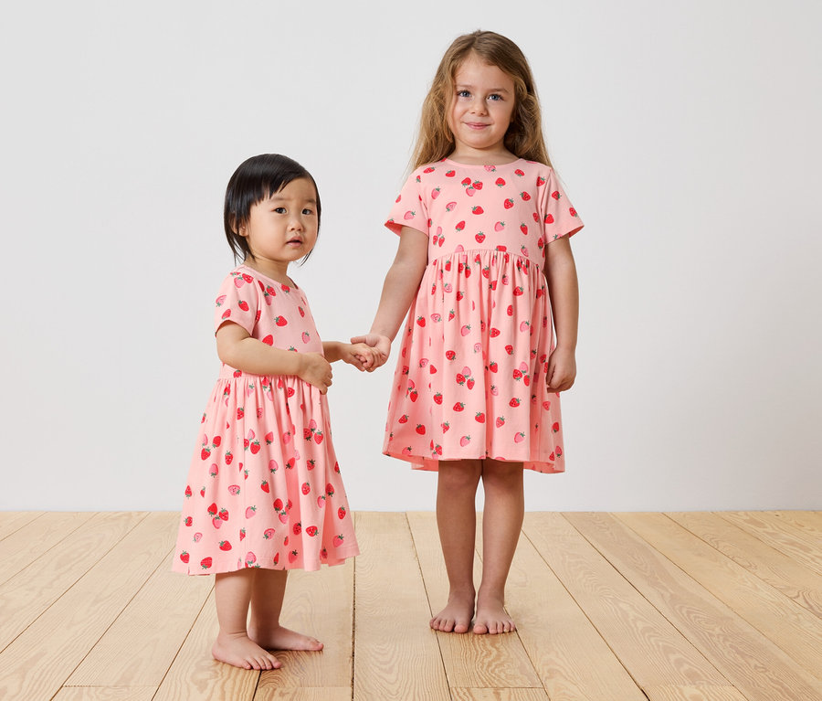 Zwei Mädchen halten Händchen und tragen rosa Erdbeerkleider.