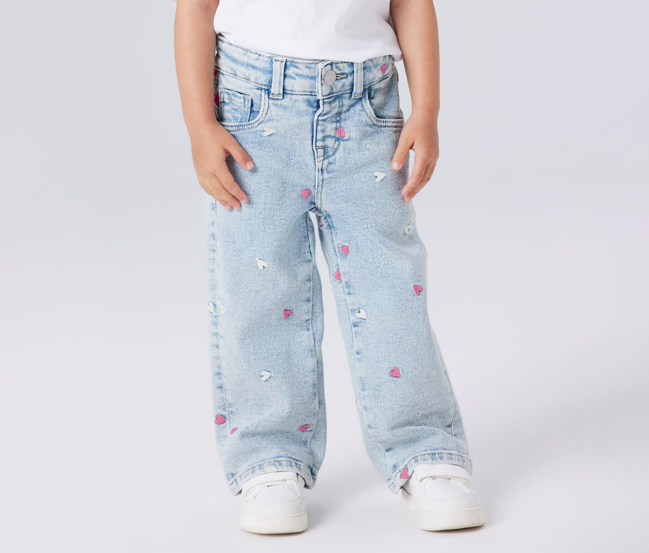 Kind trägt NAME IT Kinder-Wide Leg Jeans mit Herzchenmuster und weiße Schuhe.