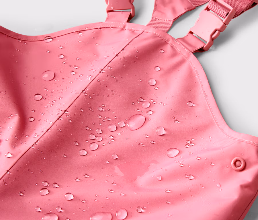 Nahaufnahme einer pinkfarbenen Regenhose mit Trägern und Wassertropfen auf dem Stoff.
