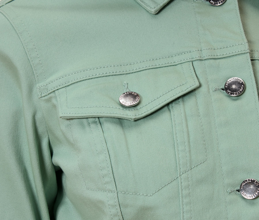 Nahaufnahme einer hellgrünen Jacke mit silbernen Knöpfen und einer Brusttasche.
