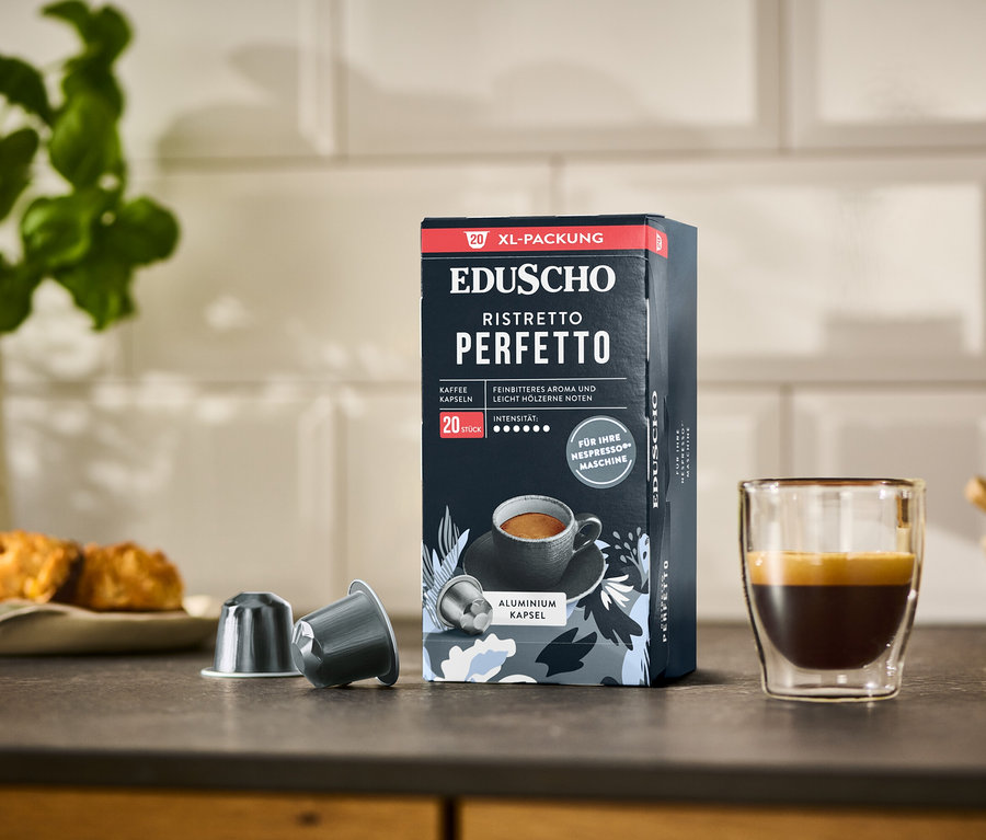 Eine Packung EDUSCHO Ristretto Perfetto Kapseln steht neben zwei Kaffeekapseln und einer Tasse Espresso.