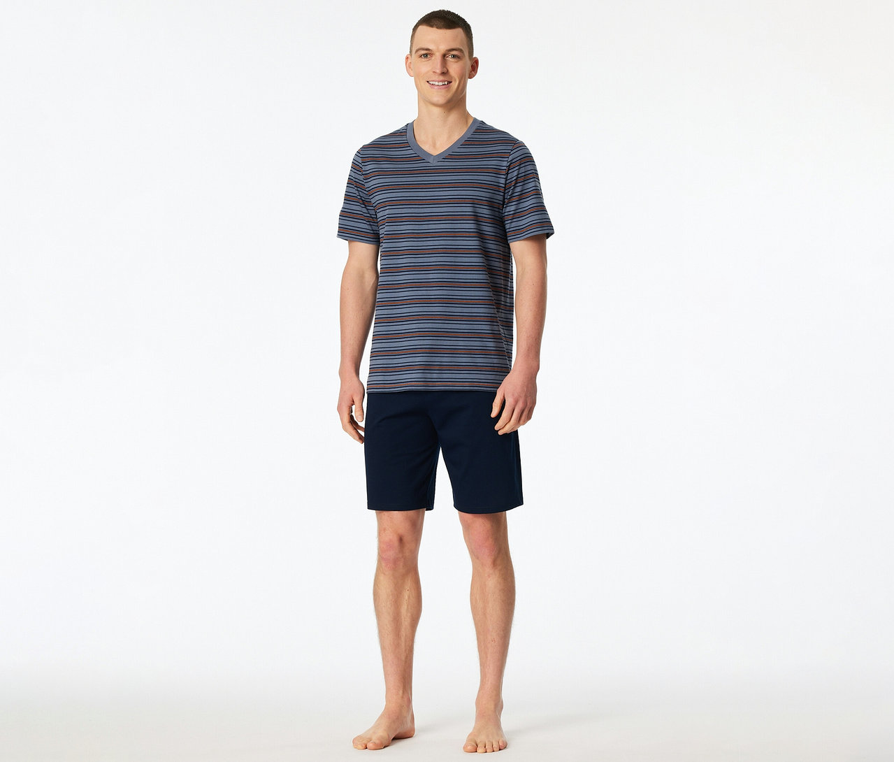Ein lächelnder Mann steht barfuß und trägt ein gestreiftes SCHIESSER Shorty-Set mit V-Ausschnitt-Oberteil und marineblauen Shorts.