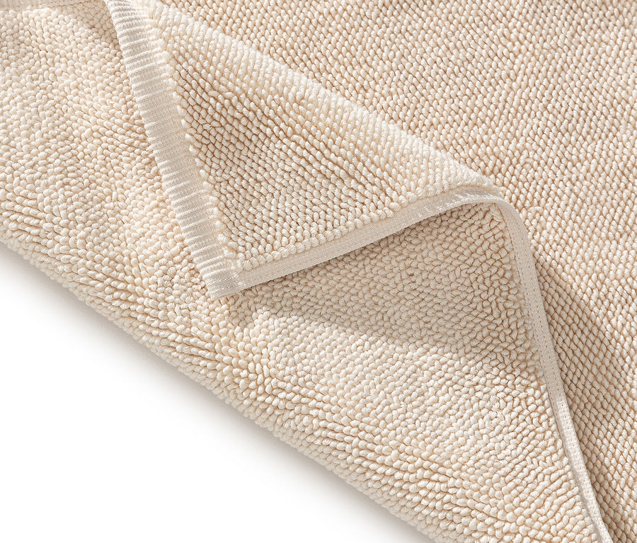 Nahaufnahme einer beigen Badematte mit umgeschlagener Ecke, die die Textur zeigt.
