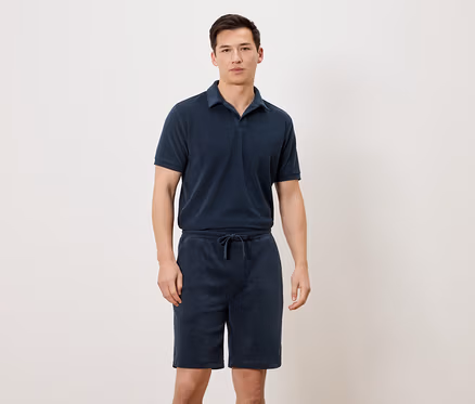 Mann trägt ein marineblaues Poloshirt und marineblaue Shorts.