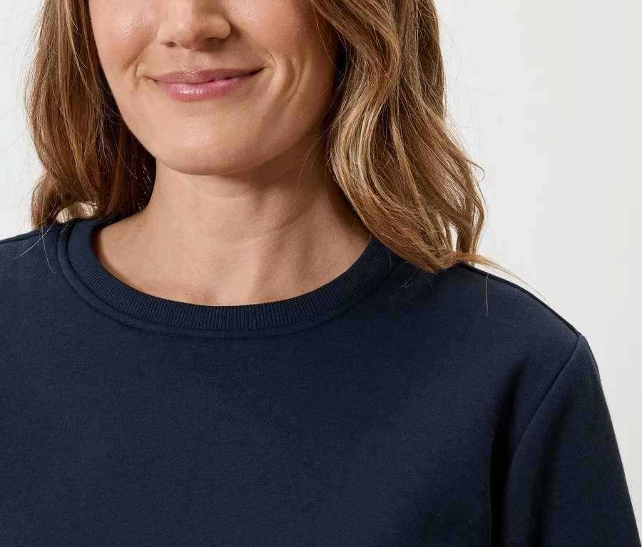 Nahaufnahme einer Frau mit blonden, gewellten Haaren, die ein dunkelblaues Sweatshirt trägt.