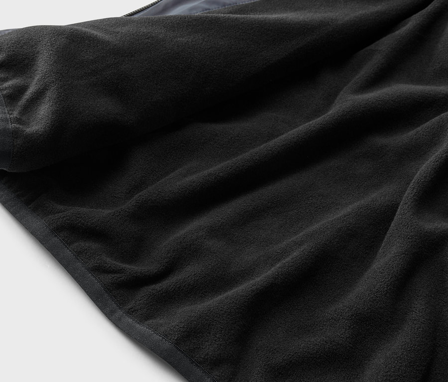 Nahaufnahme eines schwarzen Fleece-Futters mit grauem Saum auf einem hellgrauen Hintergrund.