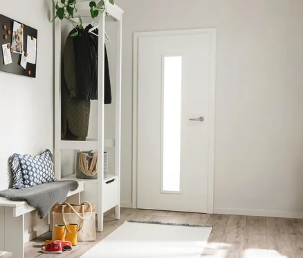 Ein heller Eingangsbereich mit weißer Garderobe und Bank, einer schwarzen Magnettafel und einer weißen Tür. An der Garderobe hängen eine grüne Steppjacke und eine schwarze Jacke. Auf der Bank liegen ein blau gemustertes Kissen und ein graues Fell. Darunter stehen gelbe Gummistiefel, rote Sandalen und eine beigefarbene Tragetasche. Auf dem Holzboden liegt ein heller benuta Läufer »Mia«, ca. 70 x 200 cm.