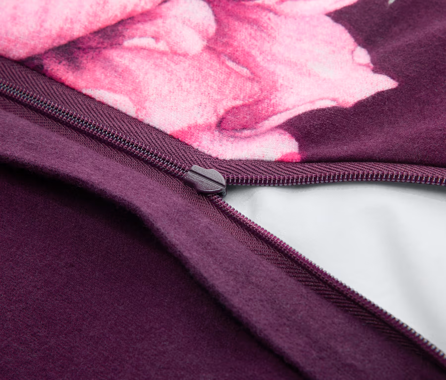 Nahaufnahme eines teilweise geöffneten dunkelvioletten Reißverschlusses auf einem Stoff, der ein weißes Futter zeigt. Der Stoff hat einen dunkelvioletten Bereich und ein rosa Blumenmuster.