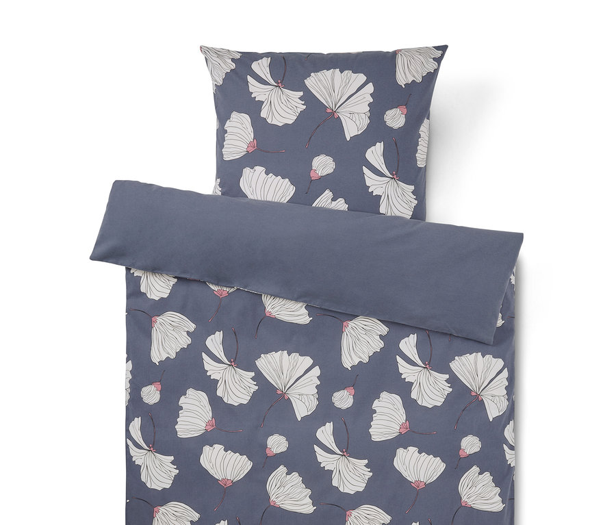 Bettwäsche-Set mit dunkelblauem Hintergrund und weißen Blüten mit rosa Akzenten. Der Kissenbezug liegt über dem Bettbezug, dessen obere Kante umgeschlagen ist und eine einfarbige dunkelblaue Rückseite zeigt.