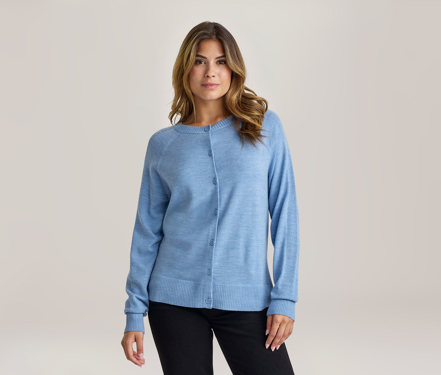 Frau mit braunen Haaren trägt einen hellblauen Strickcardigan mit Knöpfen und schwarze Hose, blickt nach vorne.